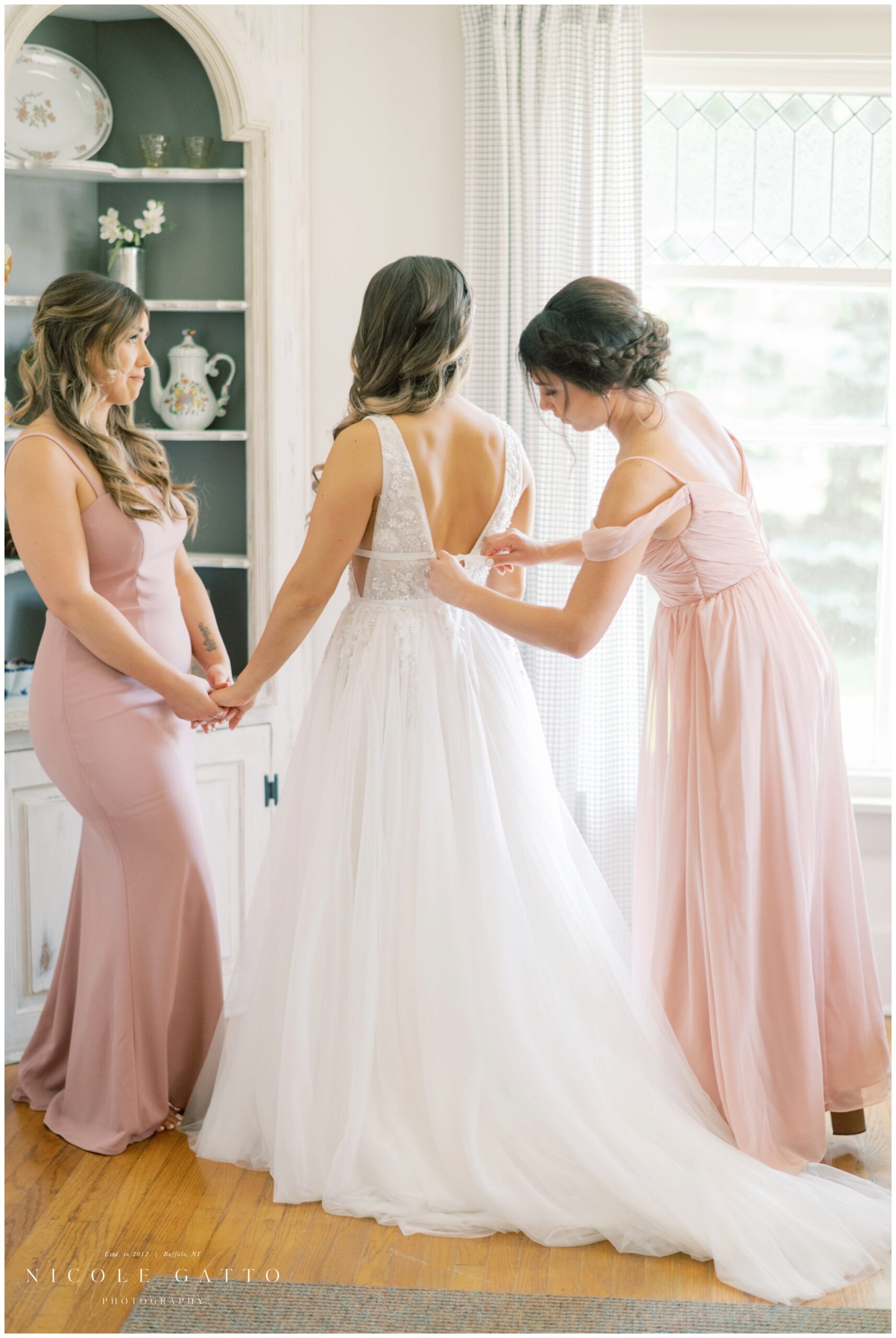 bridesmaids getting bride dressed at cottage on property at hayloft in the grove