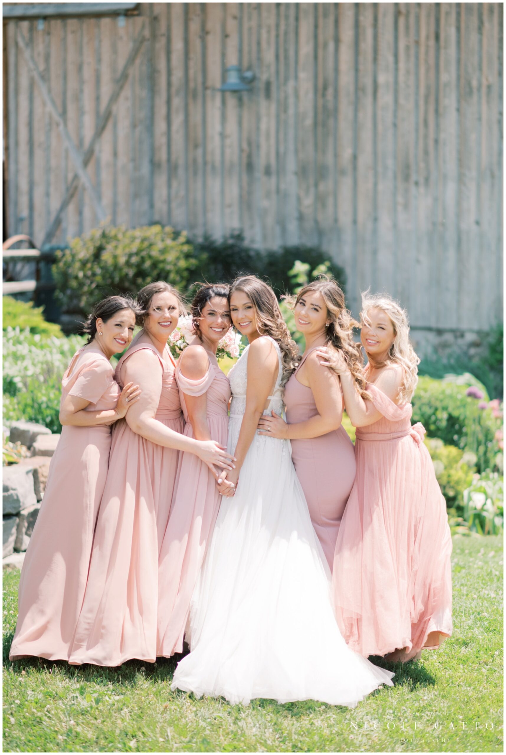 bridesmaids in pink dresses with bride in front of barn wedding at Hayloft in the grove 